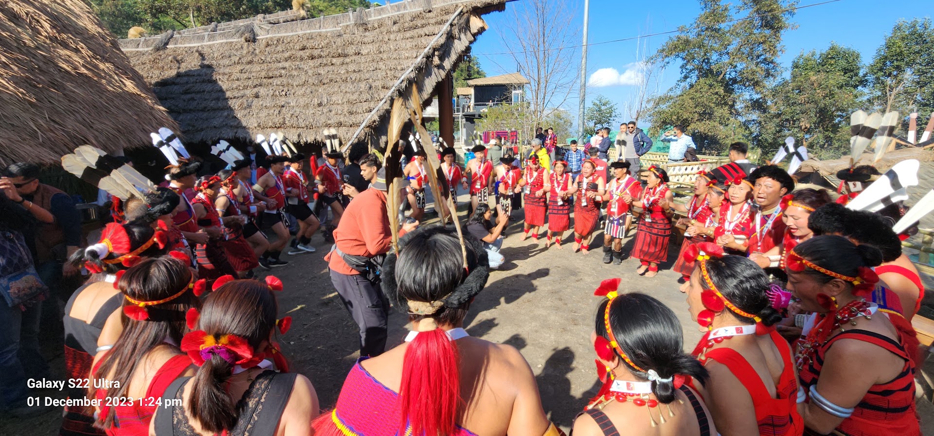 Performers in traditional clothing outside a thatched morung at Hornbill Festival