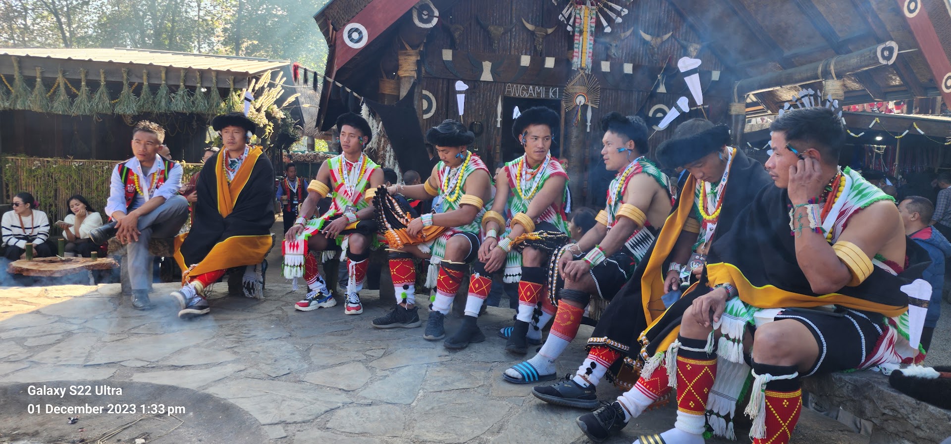Cultural performers seated outside a morung at Hornbill Festival