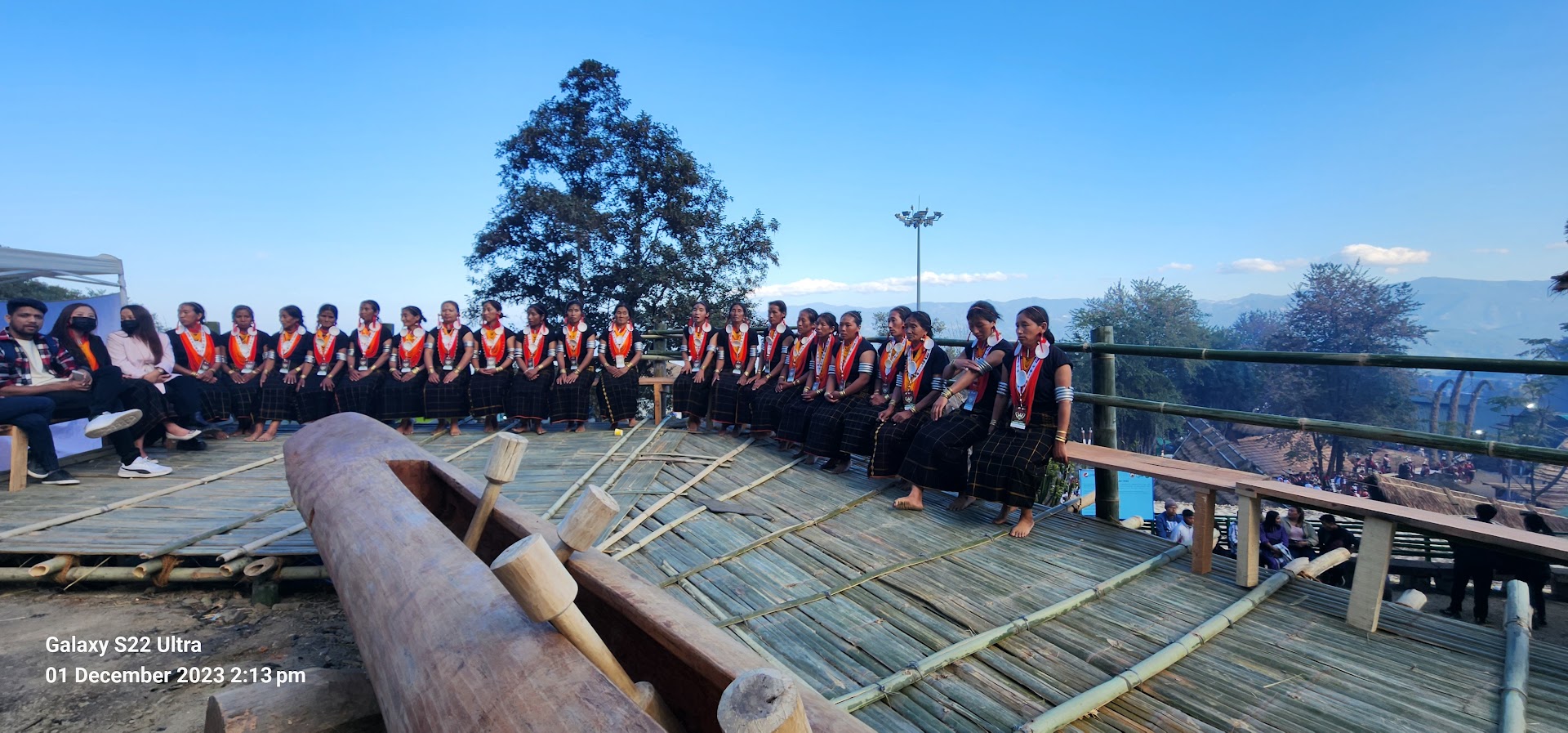 Women gathered around a log drum on a bamboo platform at Hornbill Festival